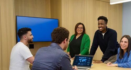 Group of colleagues having a meeting in a modern office, smiling and discussing around a table.