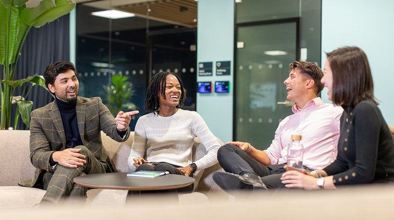 Four colleagues laughing and chatting in a lounge area.