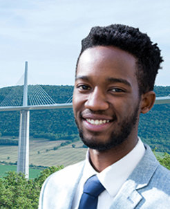 Young professional man smiling with a scenic bridge structure in the background.