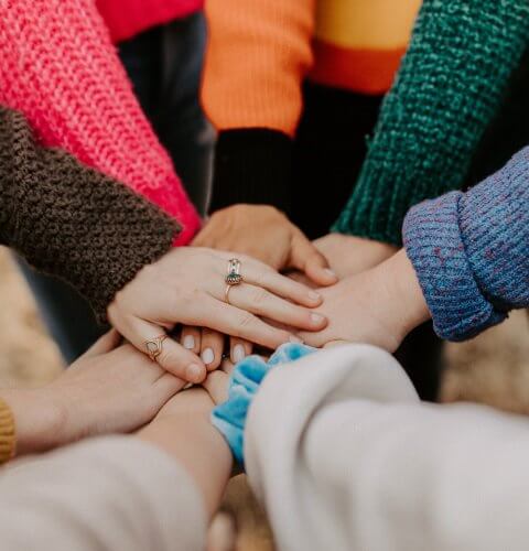 Group of diverse people placing their hands together in a show of unity and teamwork.