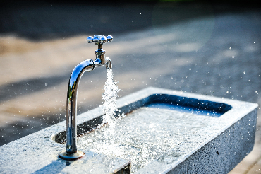 tap running clear water into a stone basin, with the water stream sparkling in sunlight