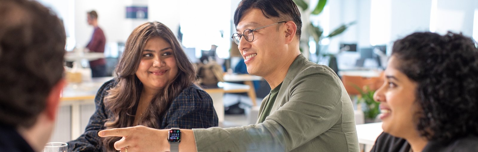 Group of coworkers sitting around a desk in a modern office, smiling and engaged in conversation.
