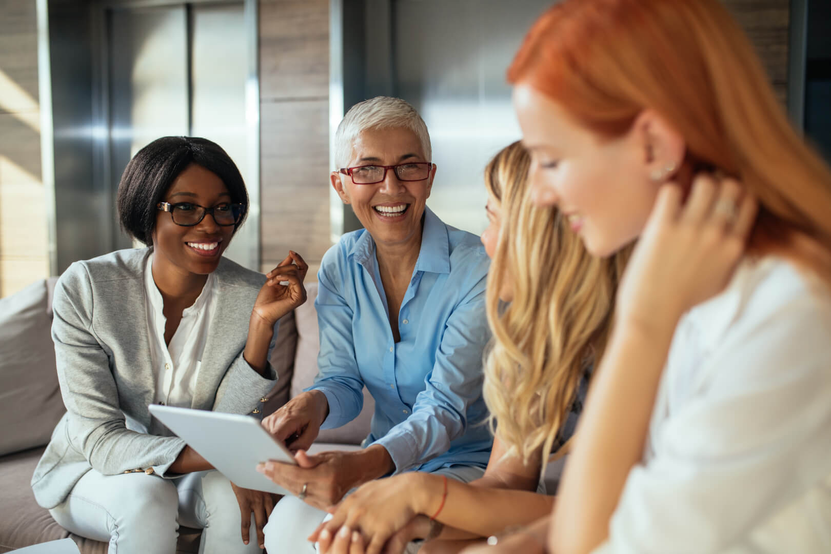 Group of professional women smiling and discussing ideas while looking at a tablet.