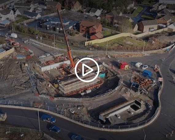 Aerial view of a construction site with a crane, building works, and nearby roads in a residential area.