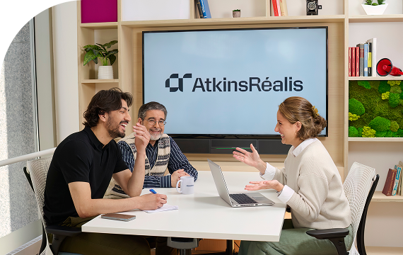 Diverse team gathered around a table in a collaborative meeting, all smiling and engaged in conversation in a contemporary workspace.