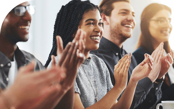 Group of diverse people sitting and clapping in a brightly lit room, appearing happy and engaged.