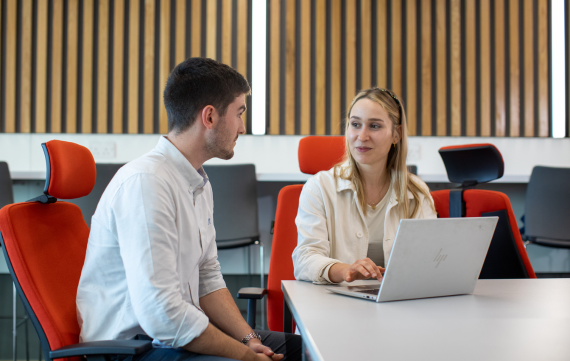 two young professionals collaborating at an office environment, with a laptop kept on a table