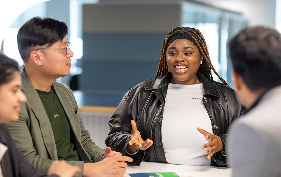 Group of diverse individuals engaged in a lively discussion at a table in a modern office environment.