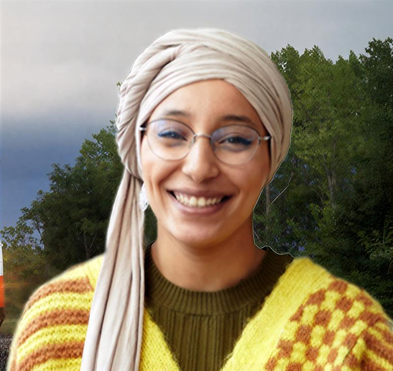 Smiling young man standing in front of an aerial view of a large, green highway interchange with a city skyline in the background