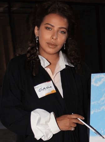 Woman wearing a black coat with a name tag, standing indoors.