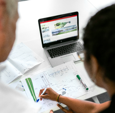 a man and a woman looking at a computer screen and  writing  on some plans