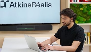 young man with moustache typing on laptop with AtkinsRéalis logo on backdrop