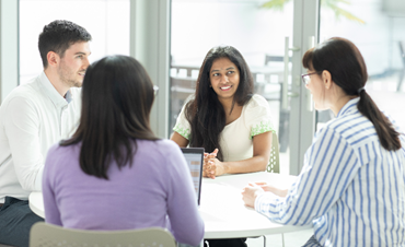 A group of employees sitting and talking to each other, one of the employees has her laptop opened in front of her