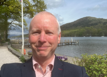 Selfie image of Brian in front of a lake and hill